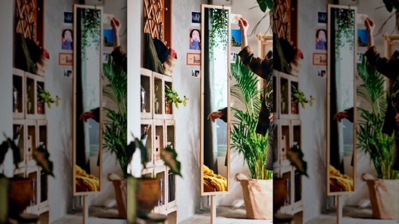 A person stands next to a floor mirror made of pine in a bohemian space