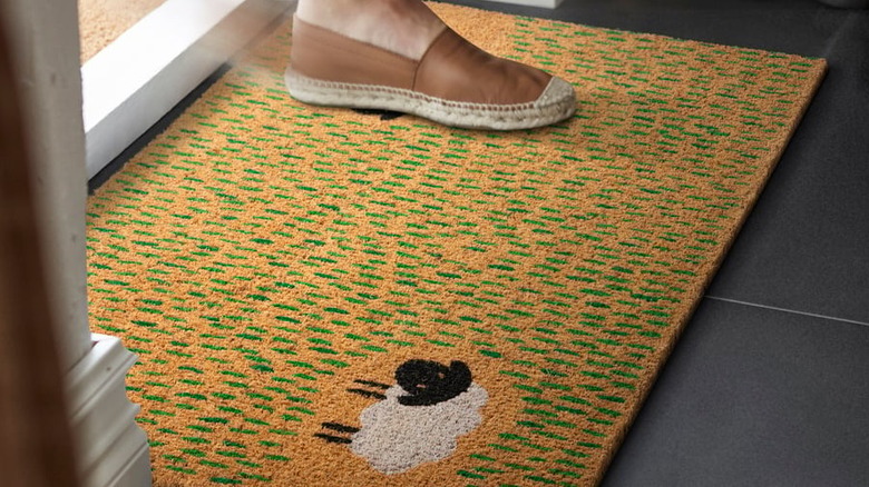 A person steps on a coir doormat decorated with a Valais blacknose sheep