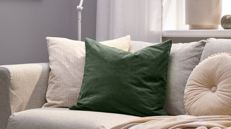 An emerald green throw pillow sits on a cream-colored couch in a neutral living room