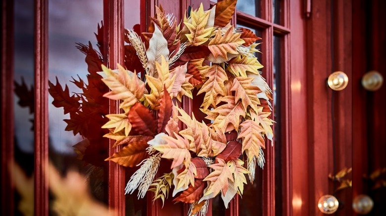 A fall wreath hangs on a red front door