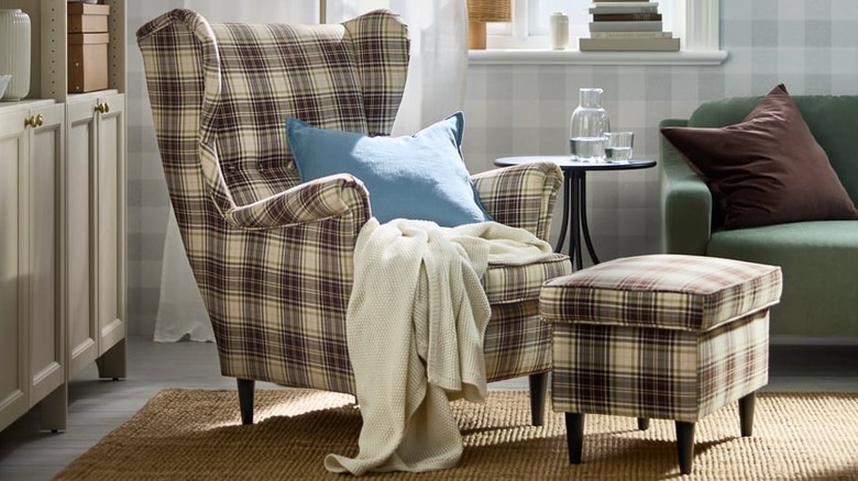 A blue pillow and cream throw blanket sit on a plaid wing chair