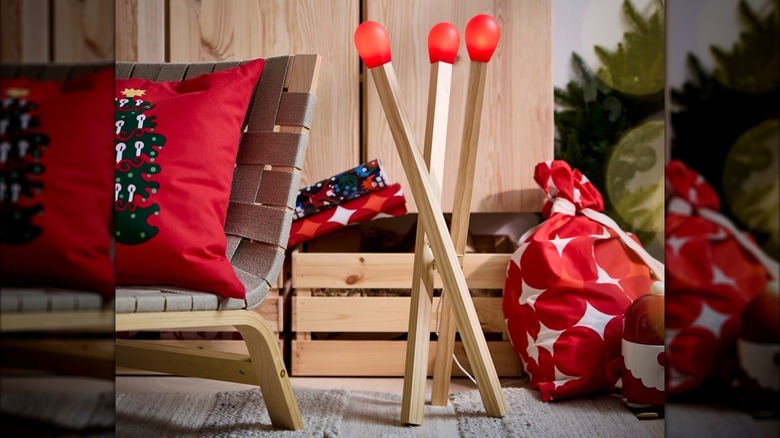 A unique matchstick-shaped floor lamp sits on a patio next to a wooden crate and deck chair
