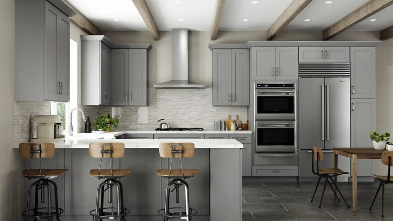 Three wood bar stools sit in front of a kitchen full of gray shaker cabinets
