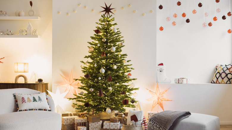 A Christmas tree sits in the center back wall of a white room full of decorations