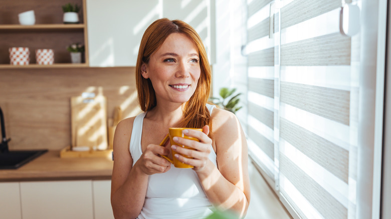 Young woman stands in kitchen next to window blinds