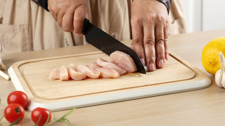 Hands cutting raw chicken on a bamboo cutting board.