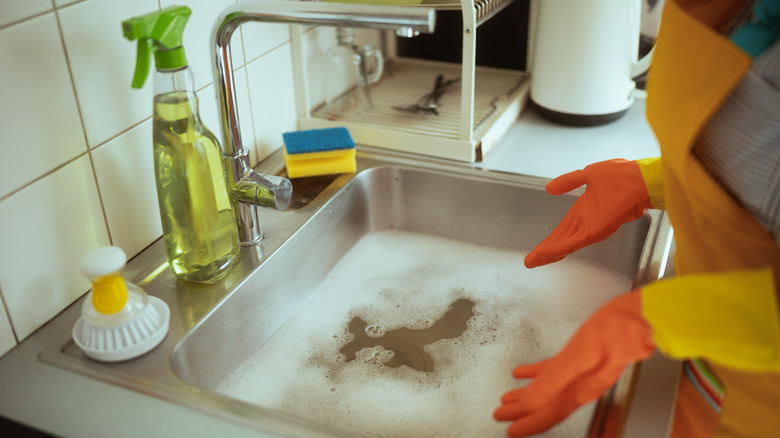 Person wearing orange gloves and looking at kitchen sink full of soapy water