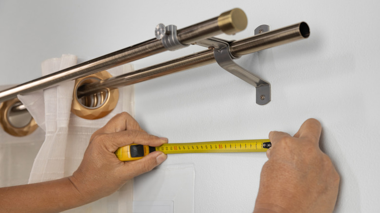 Hands measuring space under double curtain rod