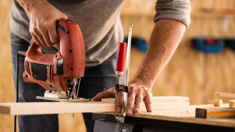 Man cross-cutting wood board with a jigsaw