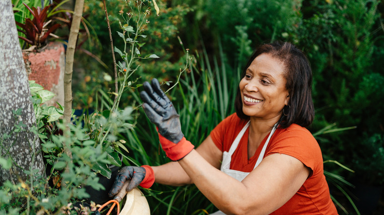 Woman with gloves and apron outside gardening with a smile on her face