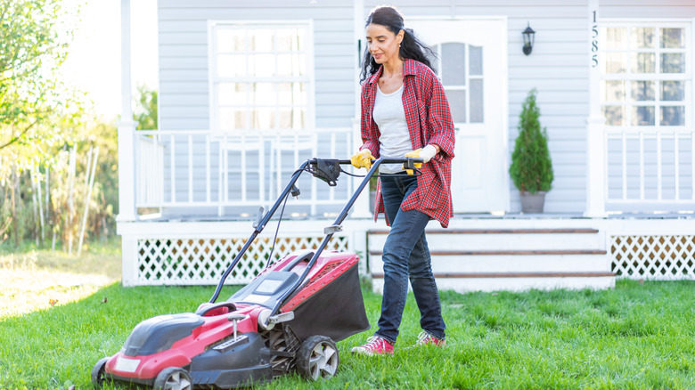 A woman in a red plaid flannel mowing her lawn with a red push mower