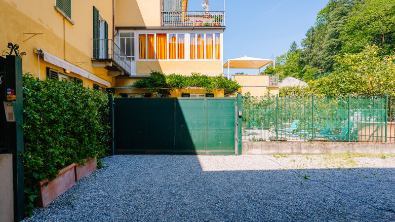 A blue gravel driveway of a yellow home with a blue gate