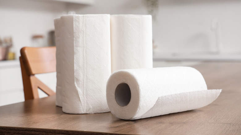 Multiple rolls of paper towels on a kitchen table, three standing up and one laying on the table