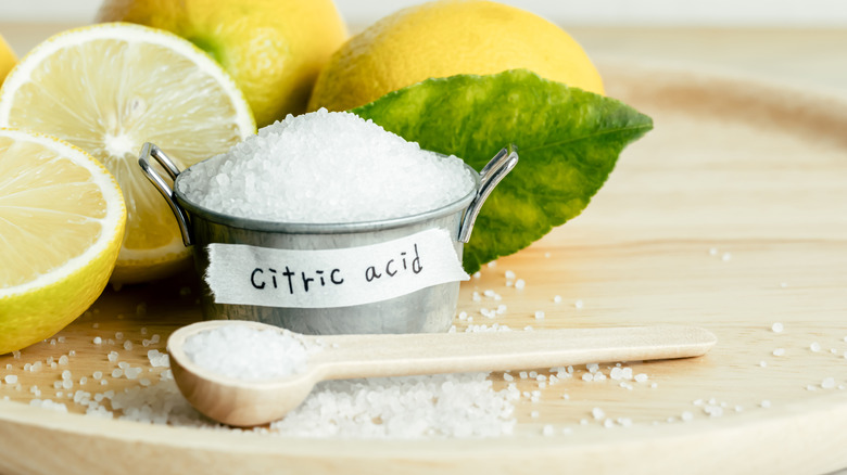 Citric acid in a bowl next to cut lemons and wooden spoon