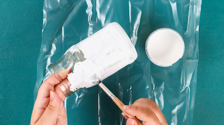 Woman brushing white paint on a Mason jar