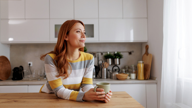 A woman holding a mug while staring out her kitchen window