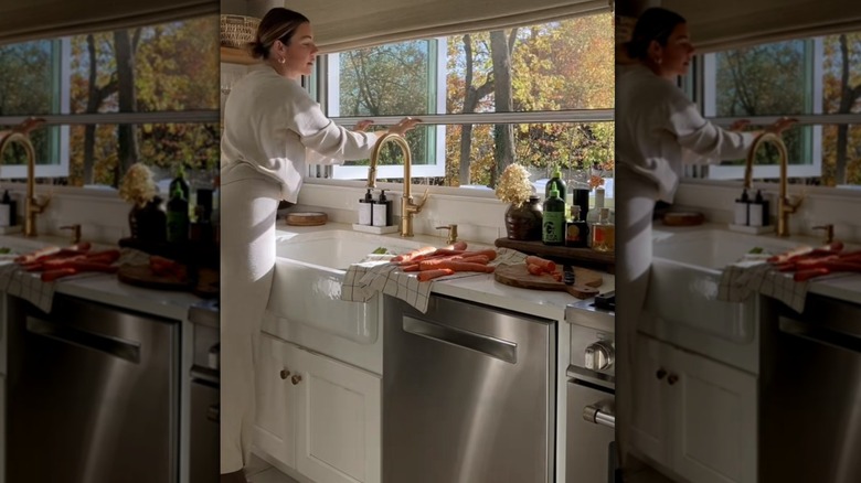 A woman pulling down a retractable bug screen from an open kitchen window