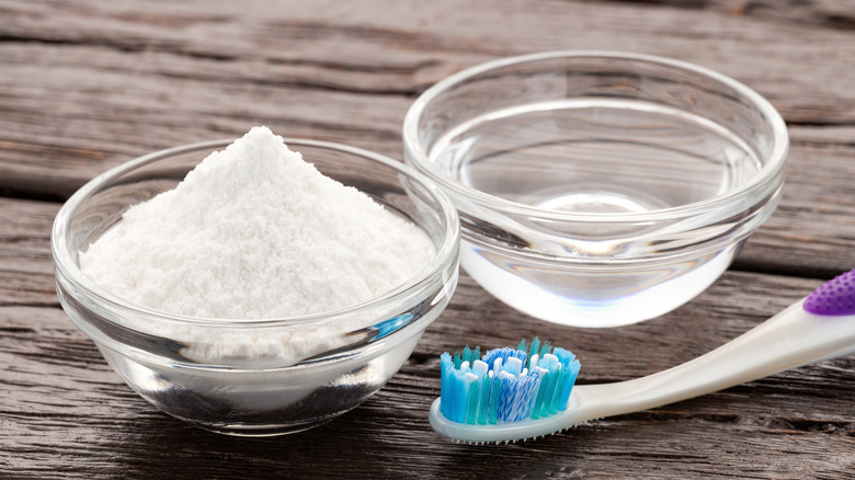 Toothbrush next to clear bowls with white powder and clear liquid