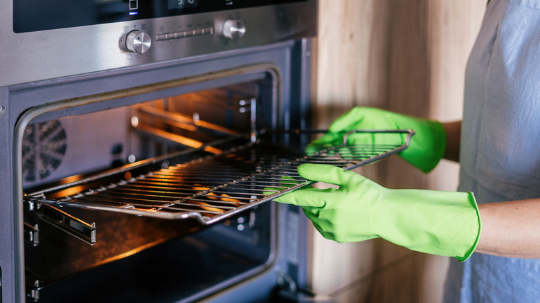 Person wearing green gloves pulling metal racks from oven