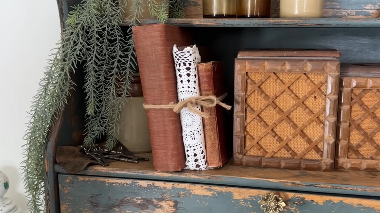 Vintage, worn books on rustic shelf with doily, twine, and other aged decor and furniture