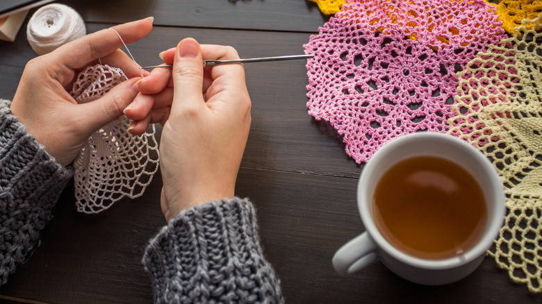 Woman crocheting different color doilies with a mug of coffee on table