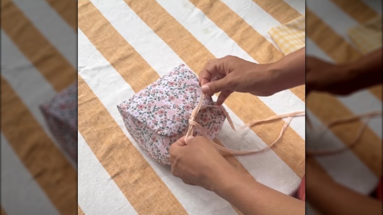 Woman tying milk jug basket storage closed with string and floral design