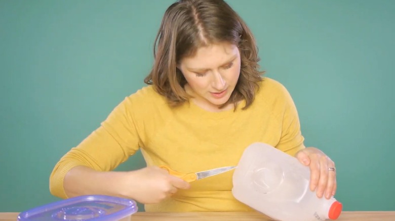 Young woman using scissors to cut up empty milk jug for DIY project over wood table