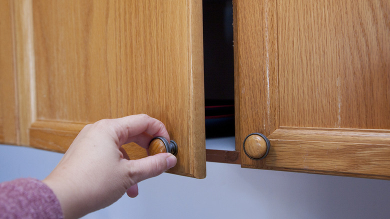 A person opening a dated brown, wood cabinet