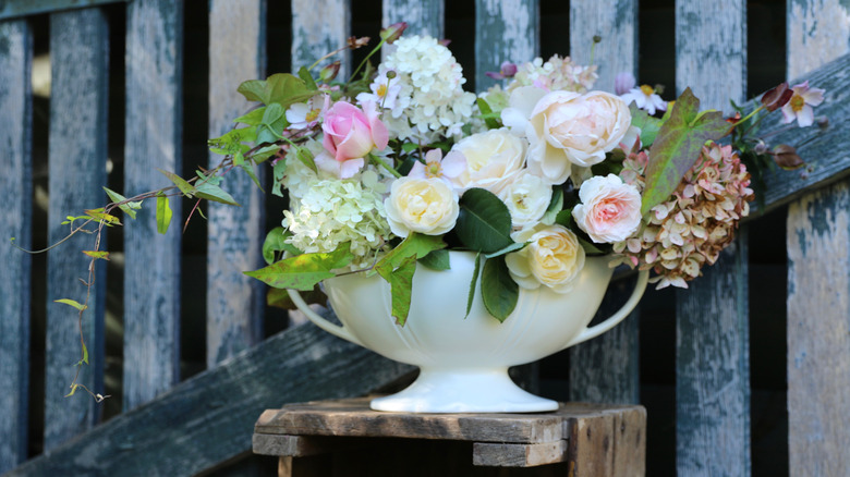Colorful cut flowers in a simple, white faience vase against a fence