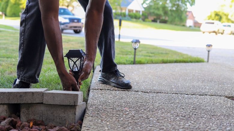 A person bends over to install a solar light near a walkway