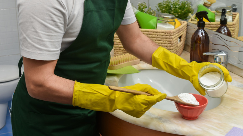 Yellow gloved hands mix up a homemade bathroom cleaner on a vanity.