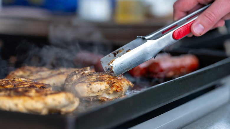 A person uses tongs to cook food on a Blackstone