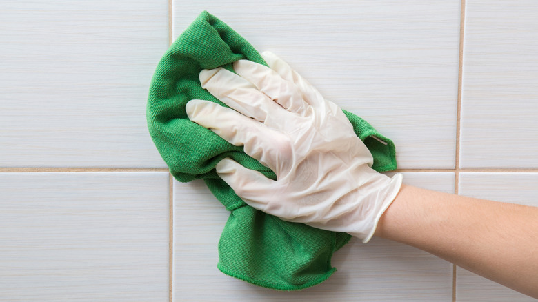 Gloved hand wiping a microfiber cloth across tile surface