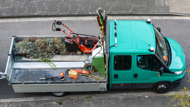 Lawnmower, wheelbarrow, broom, rake, shovels, and other tools on the bed of a truck