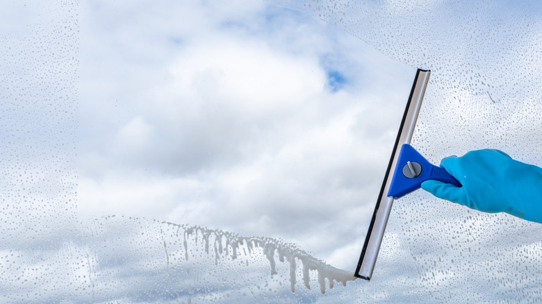 A hand running squeegee along window with cloudy sky in background