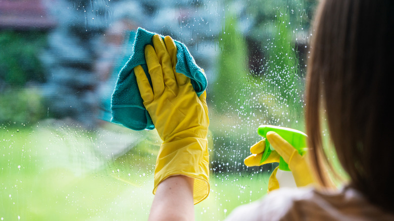 Person cleaning windows with a spray bottle solution and cloth