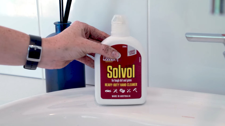 A woman with potting soil on her hand picking up a bottle of Solvol liquid soap