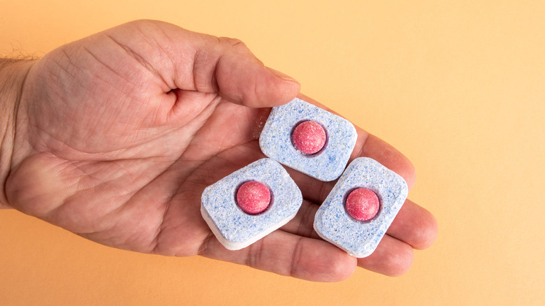Hand holding three dishwasher powder tablets