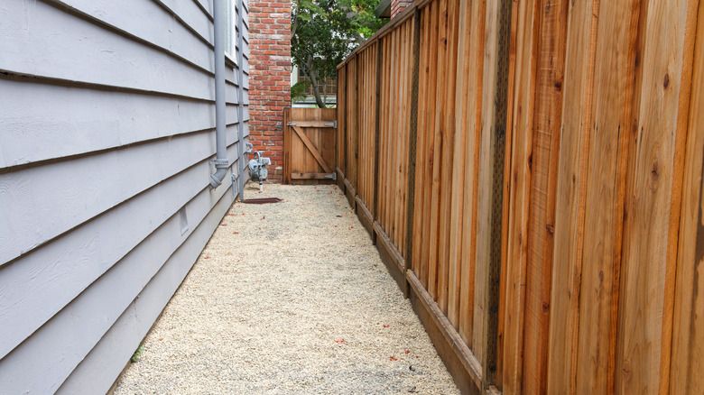 A long pea gravel path is between a gray house and wooden fence
