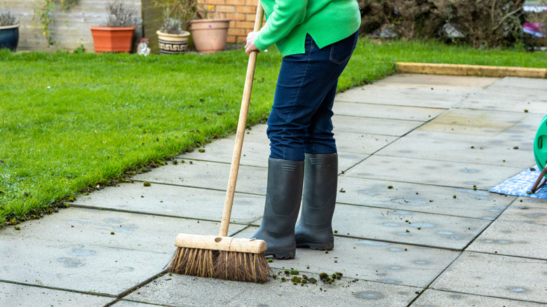 Homeowner sweeping away weeds from patio