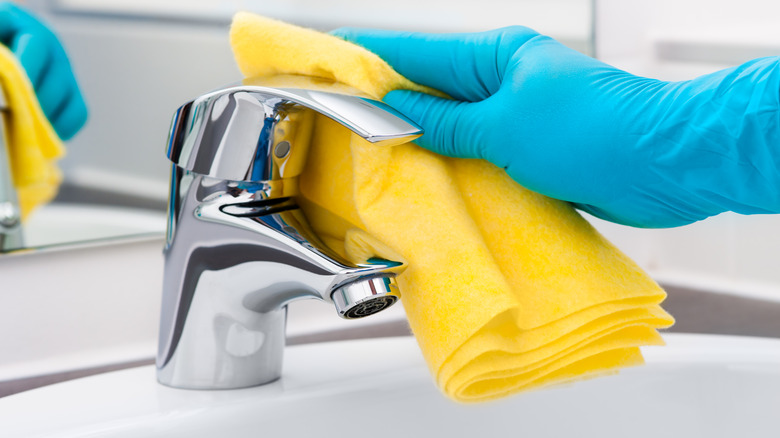 Gloved hand wiping a tap with a yellow microfiber cloth