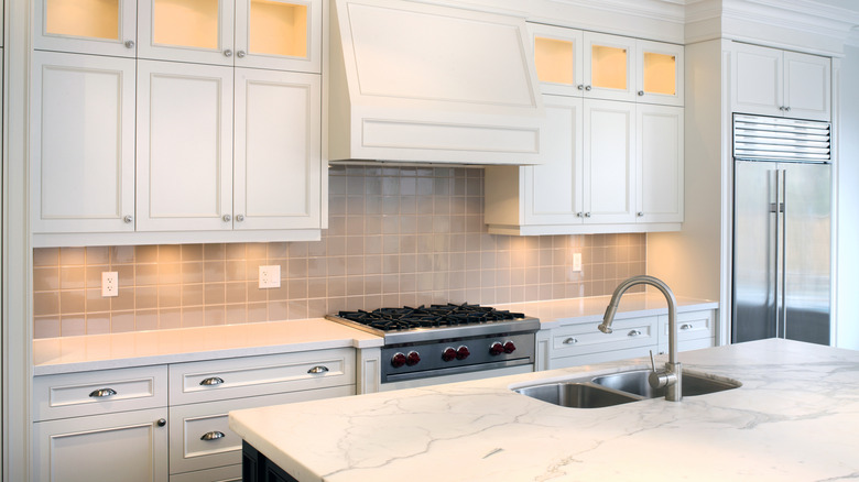 A modern kitchen with white cabinets and under-cabinet lighting glowing on the backsplash