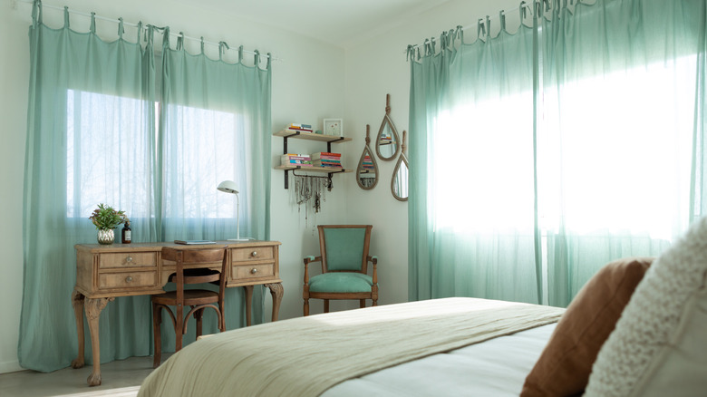 A bedroom with close-to-ceiling aqua-colored sheer curtains over the windows