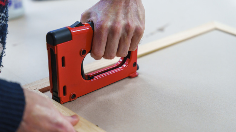 a hand is using a staple gun to staple a material to a wooden frame