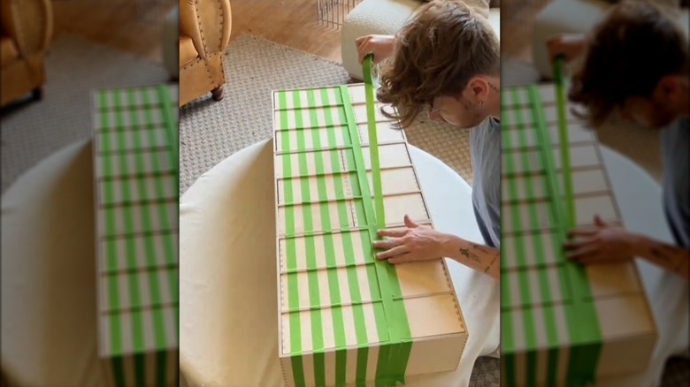 Young man using painters tape to stain IKEA cabinet for DIY project