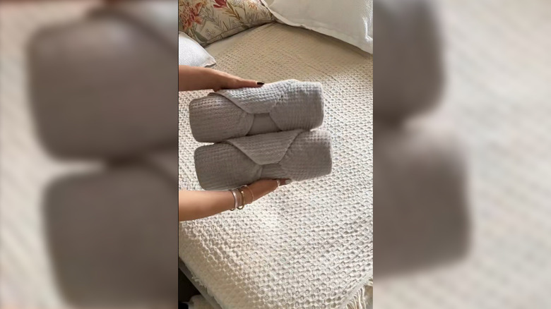Hands holding two folded towels over a bed.