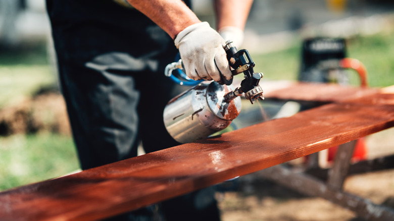 Man with gloves spraying paint over unfinished lumber outdoors for DIY project