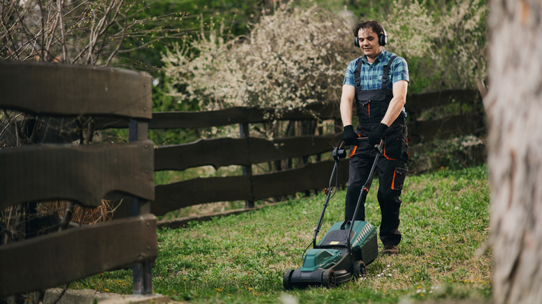 Man pushing a lawn mower between a tree and a fence