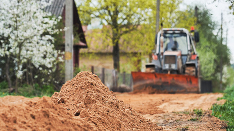 Tractor grading a dirt road behind gravel piles.