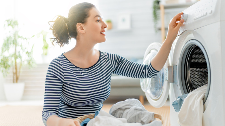 A woman smiles while loading a washing machine with clothes.